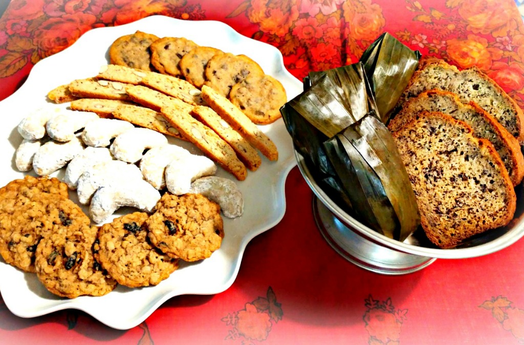 In the platter from the top down: chocolate chip cookies, almond biscotti, walnut crescents, and oatmeal cookies. In the bowl: banana bread and steamed sticky rice with bananas in banana leaves.
