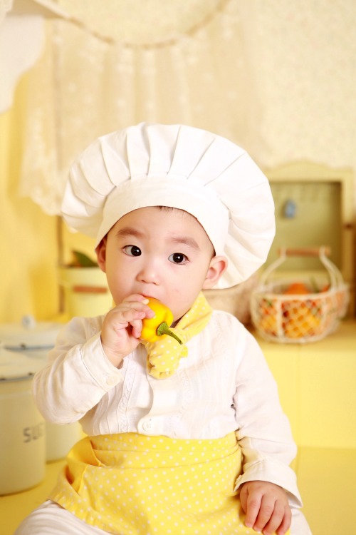 Boy dressed in chefs hat eating a vegetable Weaning your Baby for the first Time