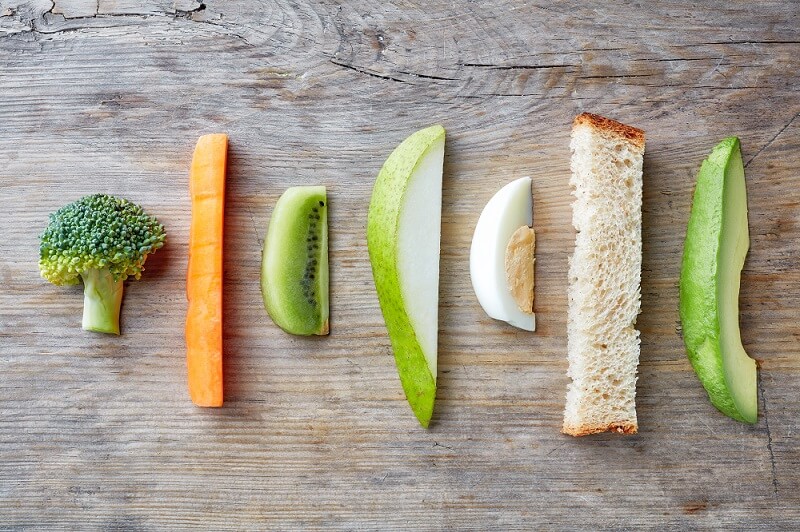Slices of starter foods such as carrot, broccoli, bread, and kiwi for baby led weaning.