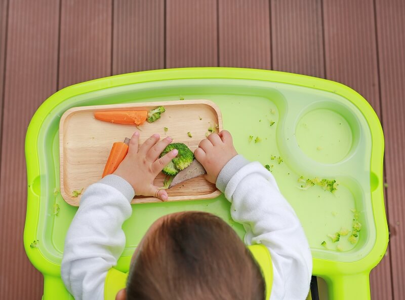 Baby sitting on high chair and grab solids foods during baby led weaning.