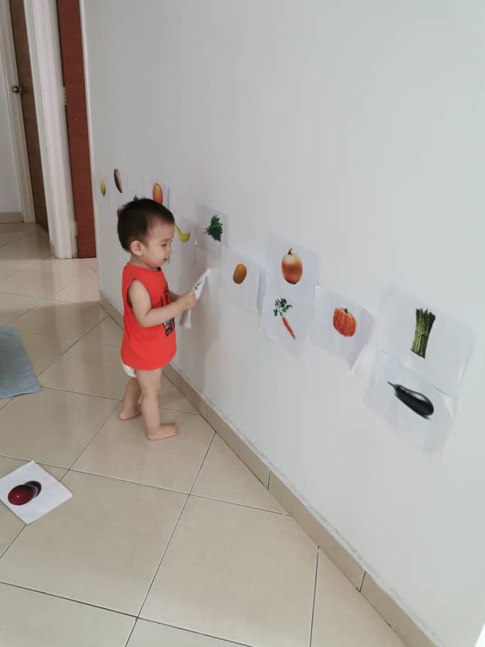 Yan Kai taking a good look at the pictures of vegetables on the wall before matching them with real vegetables.