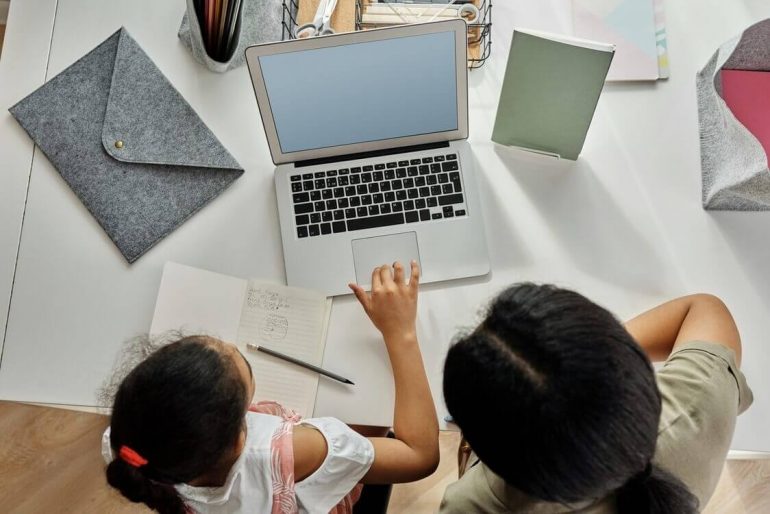 A mother is guiding her daughter with her homework by using a laptop