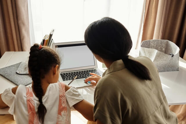 A mother is sitting beside her daughter to help her with her homework