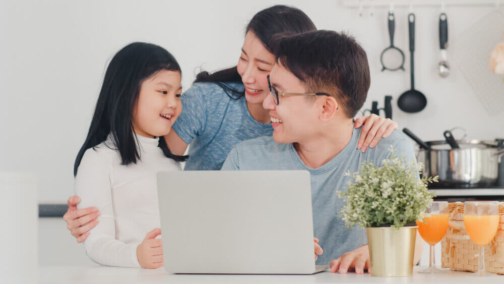 The parents are smiling to their daughter in front of a laptop.