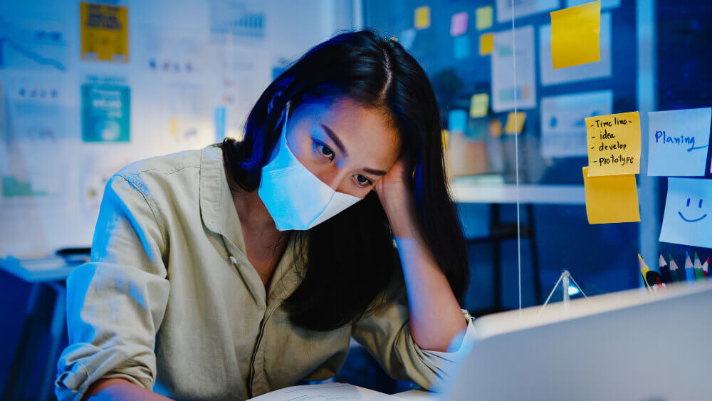 A working woman is feeling stressed over her work with a mask on.