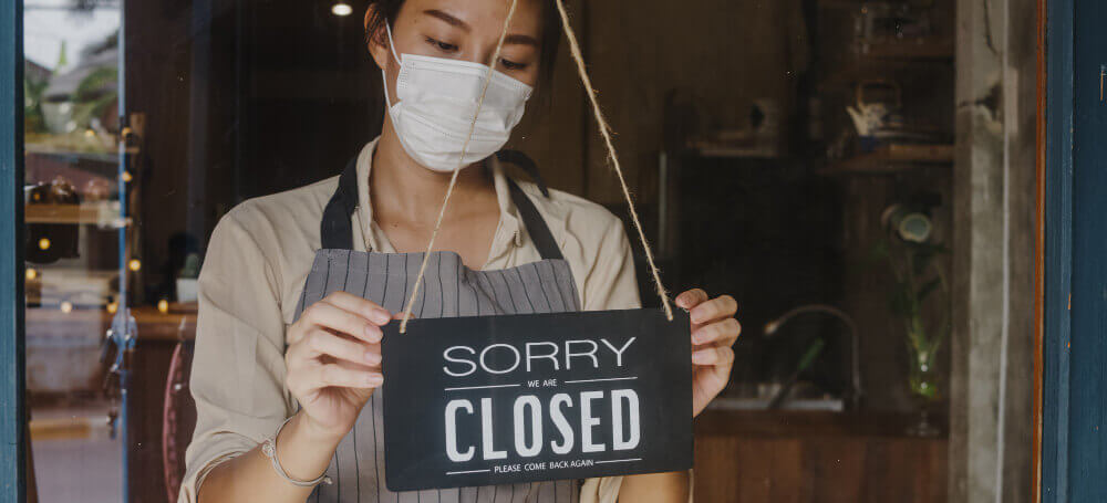 A young man is turning the closed sign in the café. (Photo credit: Freepik))
