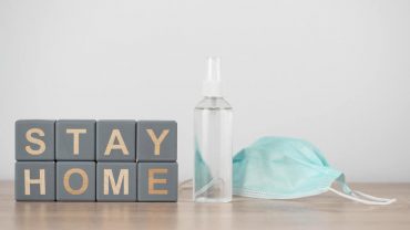 Sanitizer and face mask are placed next to the wooden cubes stating 'stay home'.