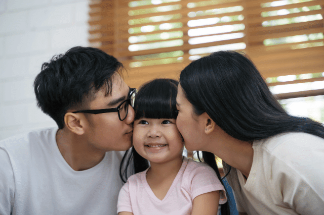 A girl is happy receiving kisses from her parents.