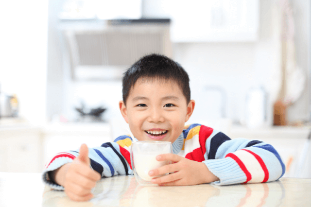 An Asian boy is showing a thumb up happily after drinking a glass of milk.