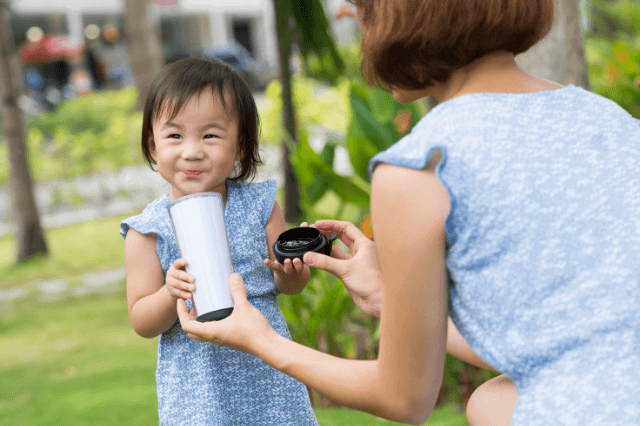 An Asian toddler is drinking a bottle of milk.