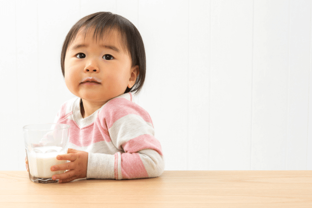 An Asian toddler is holding a glass of milk.