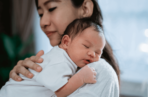 A newborn is sleeping on his mother's shoulder.