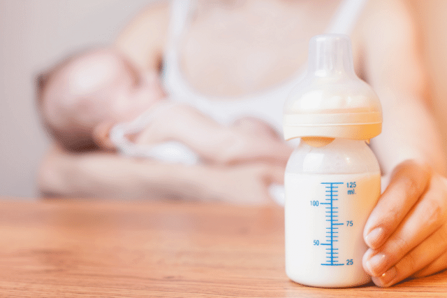 A breastfeeding mother is showing a bottle of breast milk on the table.