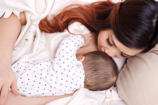 A mother is hugging her baby while breastfeeding on a bed.
