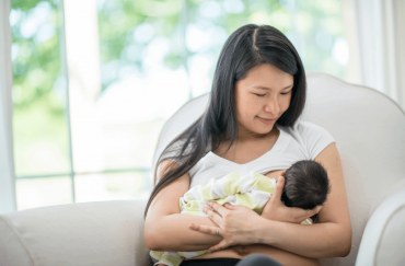 An Asian mother is breastfeeding her baby on the sofa.