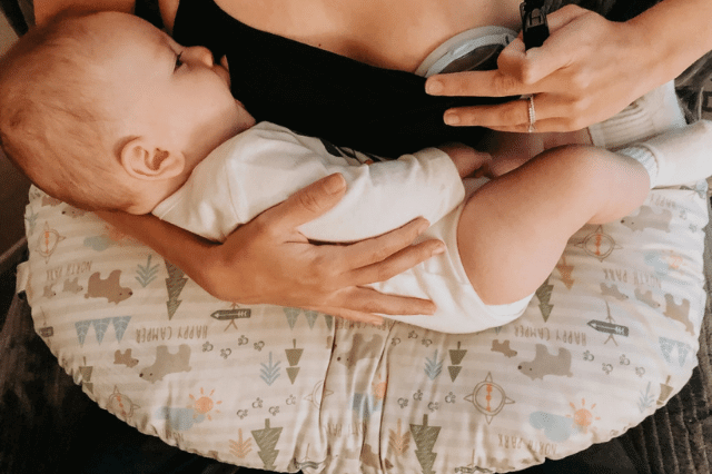 A mother is having a lacti-cup on one side of her breast while breastfeeding her baby.