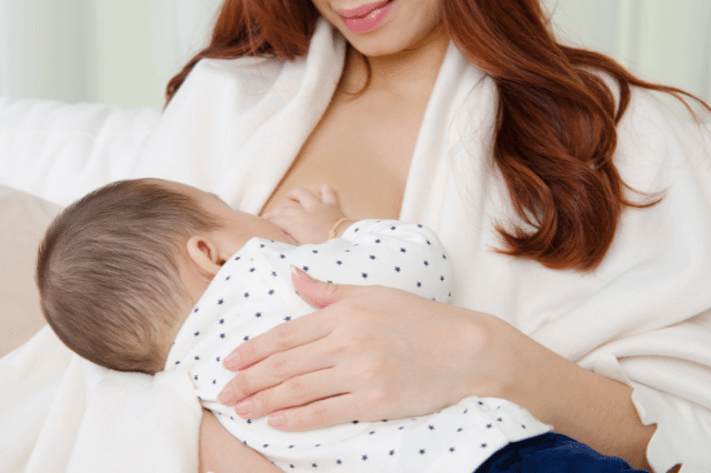 A mother is tapping her baby while breastfeeding.