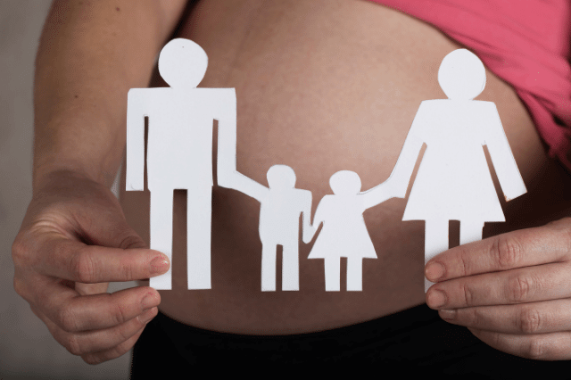 A pregnant woman is holding a paper cutout of a family after conceiving.