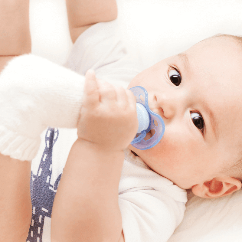 A two-month old baby is having a pacifier in his mouth.