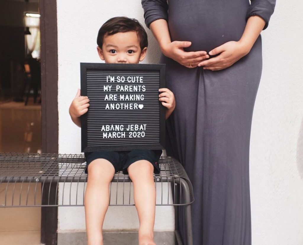 A boy is holding a board with his pregnant mother.