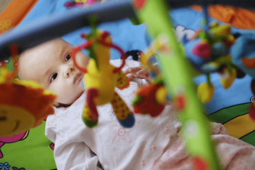 A four-month-old baby is lying down with a hanging toy on top of her.