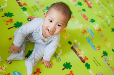 A seven-month-old baby is sitting on a play mat happily.