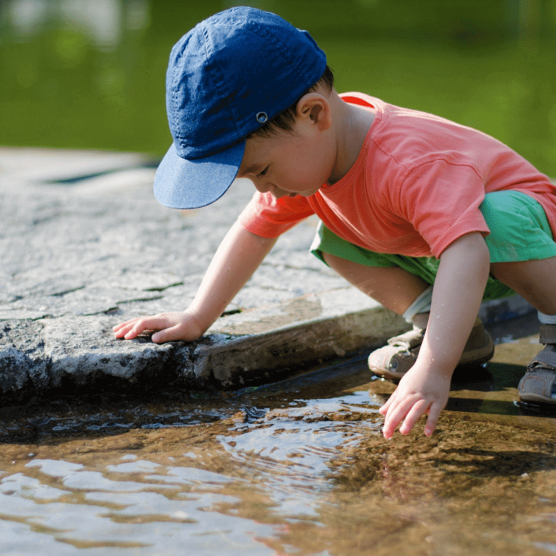 A boy is curiously feeling the water at the river bank.