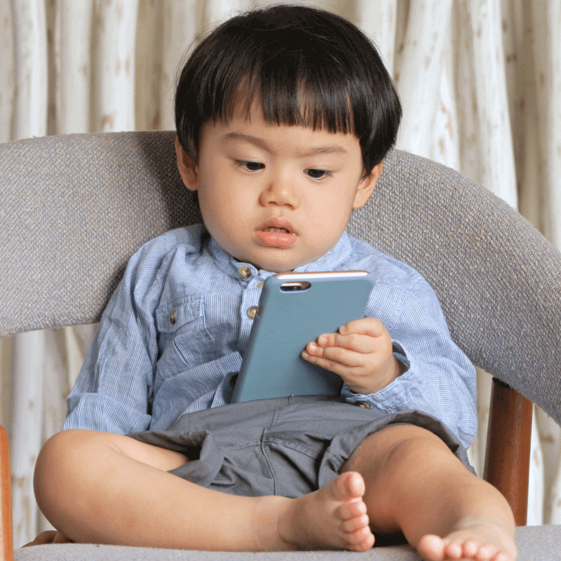 A toddler is staring at a phone on a chair.