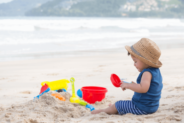 A 12-month-old Asian baby boy is playing sand on the beach.
