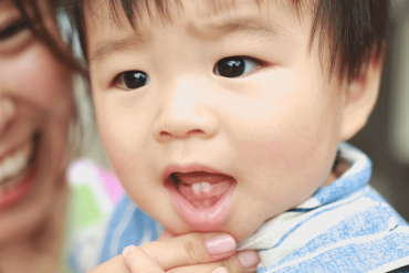A cute Asian baby is showing his first baby teeth.