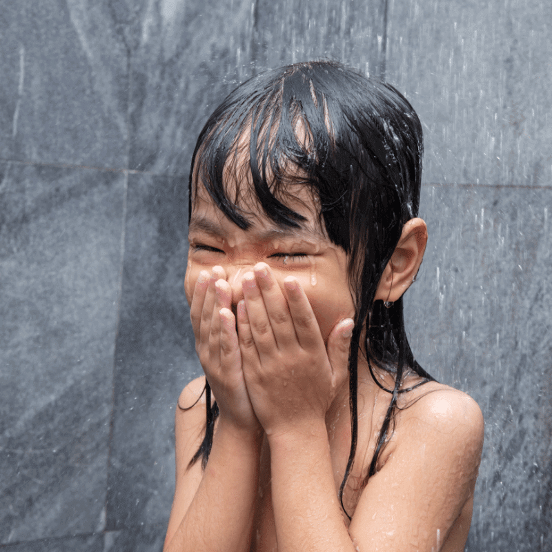 A Chinese little girl is taking a shower in the bathroom.