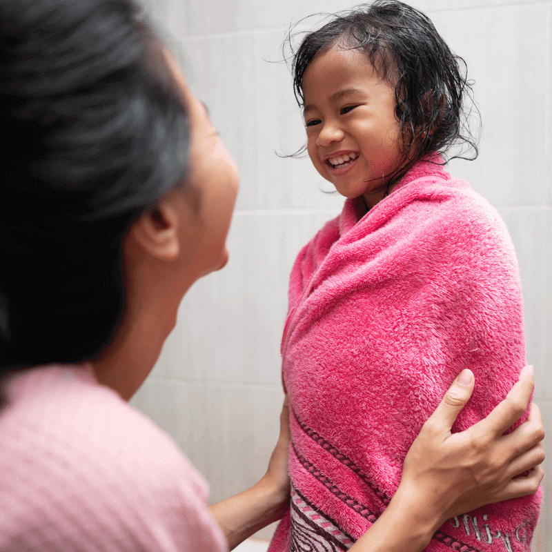 A happy young girl is being dried by her mother with a towel.