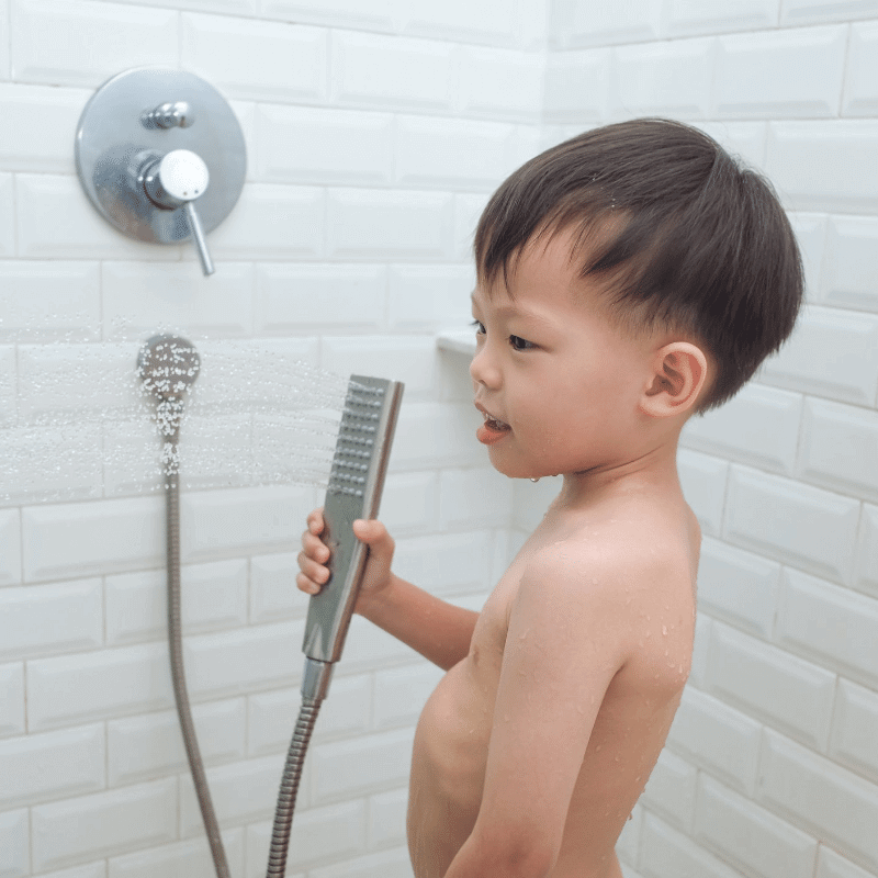 A cute little Asian toddler is taking a shower by himself.