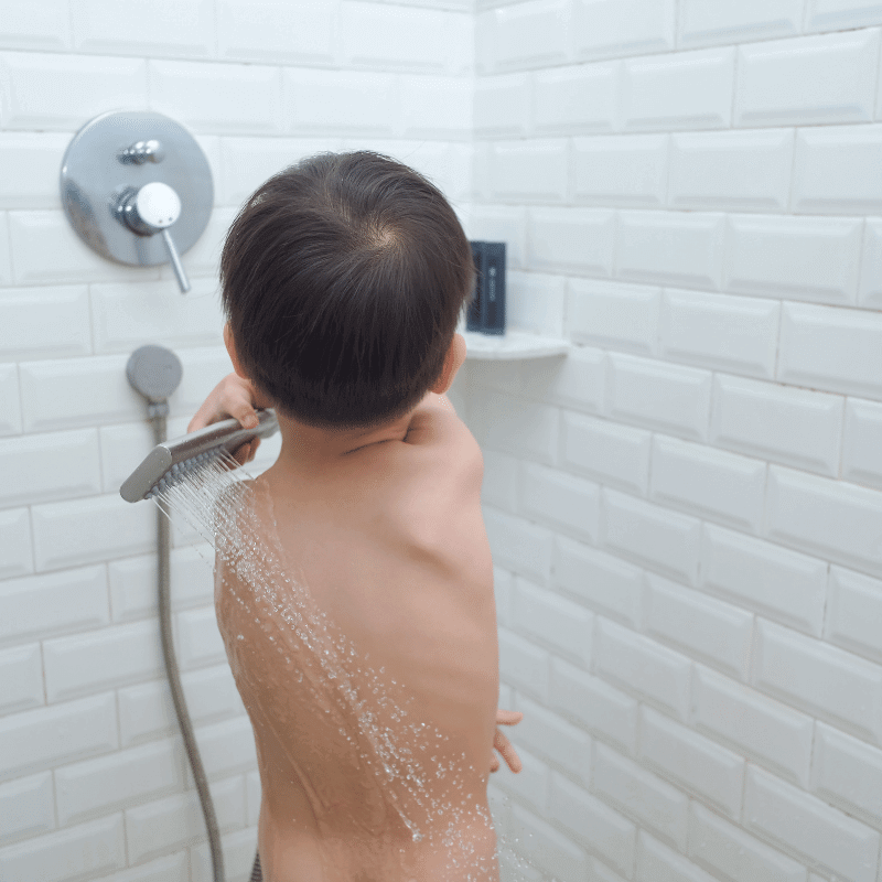 A three-year-old boy is taking a shower by himself.