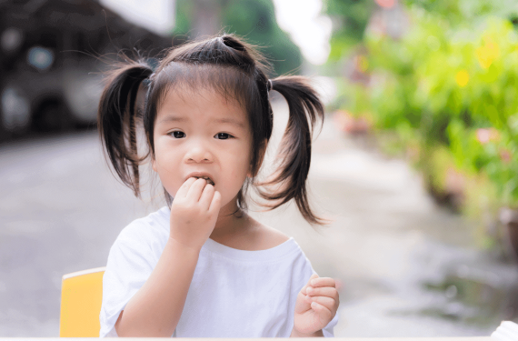A 15-month-old Asian toddler is eating fruits in front of her house.