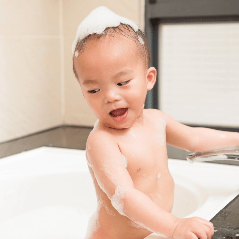 An Asian toddler is having some bath foam on his body.
