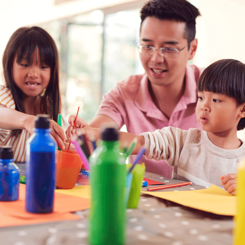 An Asian father is having fun doing art with his children.