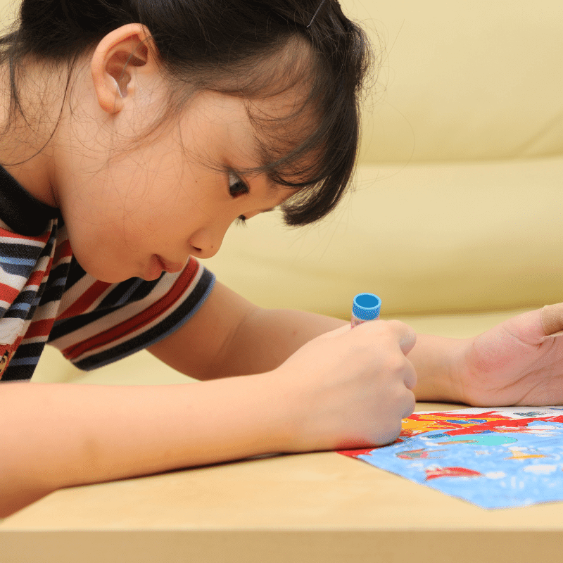 A little girl is colouring a picture with a blue crayon.