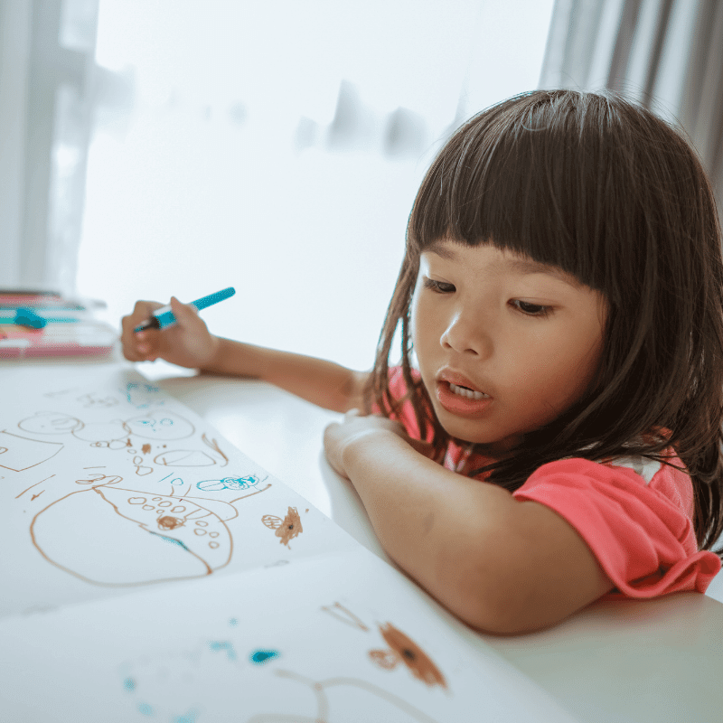 A little girl is drawing on a piece of blank paper.