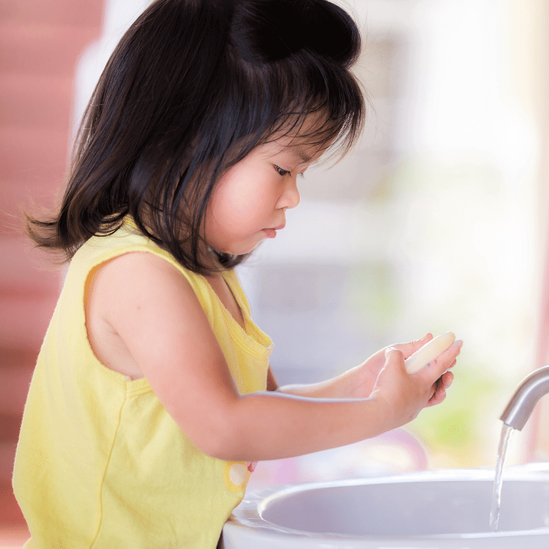 A little girl washing hands with soap in the bathroom.