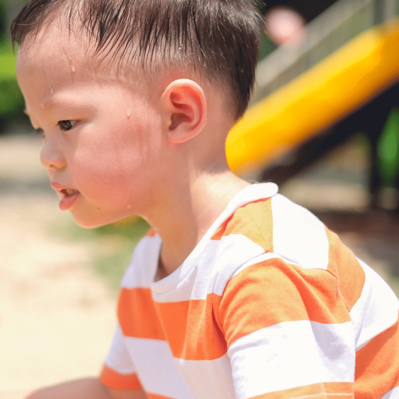 An Asian boy is sweating while playing in the playground.
