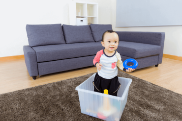 An Asian toddler is playing happily in a transparent box at home.