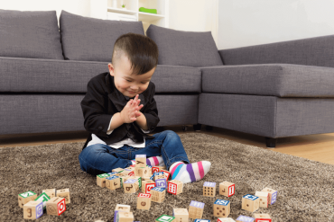 An Asian toddler is playing with the wooden blocks in the living room.