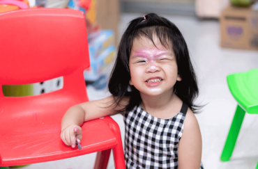 A 23-month-old toddler is winking with some glitter on her forehead.