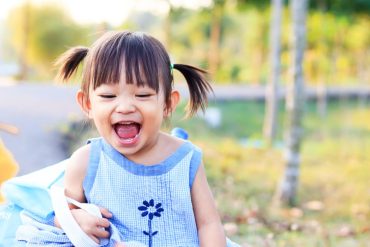 An Asian toddler is playing outdoors happily.