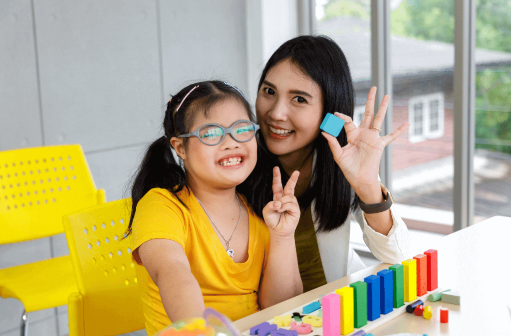 A girl with Down syndrome is learning happily with her teacher in a classroom.