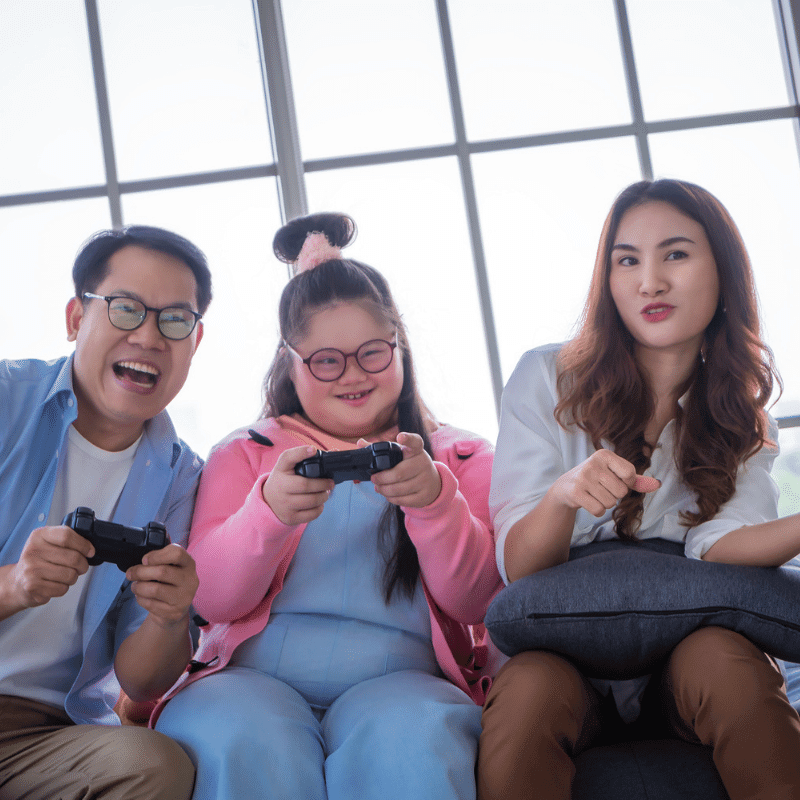 A girl with Down syndrome is having fun playing video games with her parents.