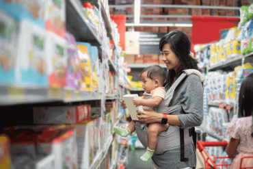 An Asian mother is buying items while carrying her baby daughter.