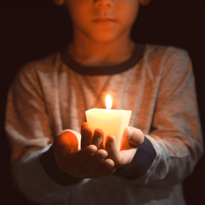 An Asian boy is holding a candle in his hands in the dark.