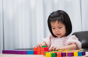 An Asian toddler is playing with the building blocks on the table.